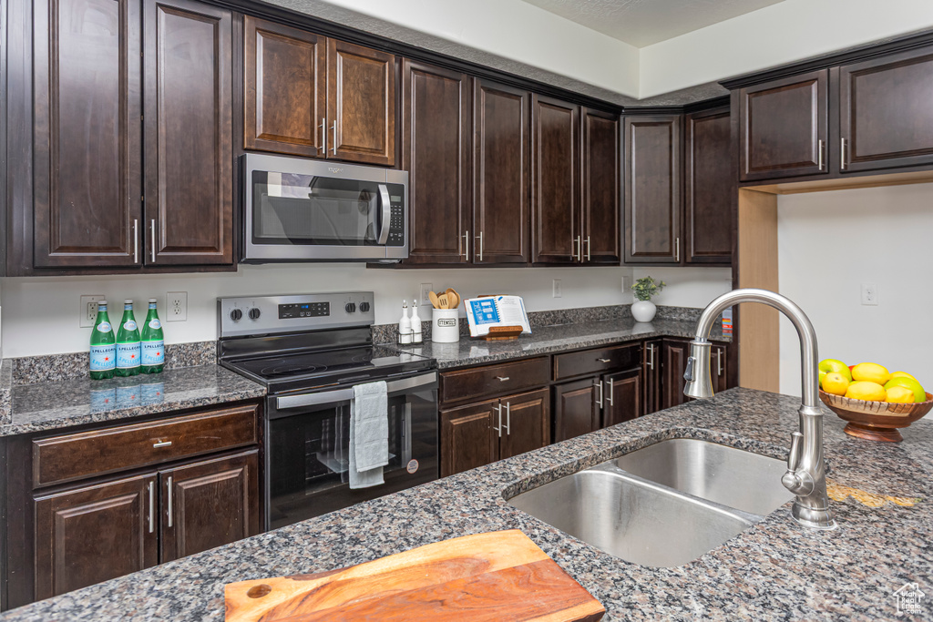 Kitchen with dark stone countertops, dark brown cabinetry, stainless steel appliances, and a sink