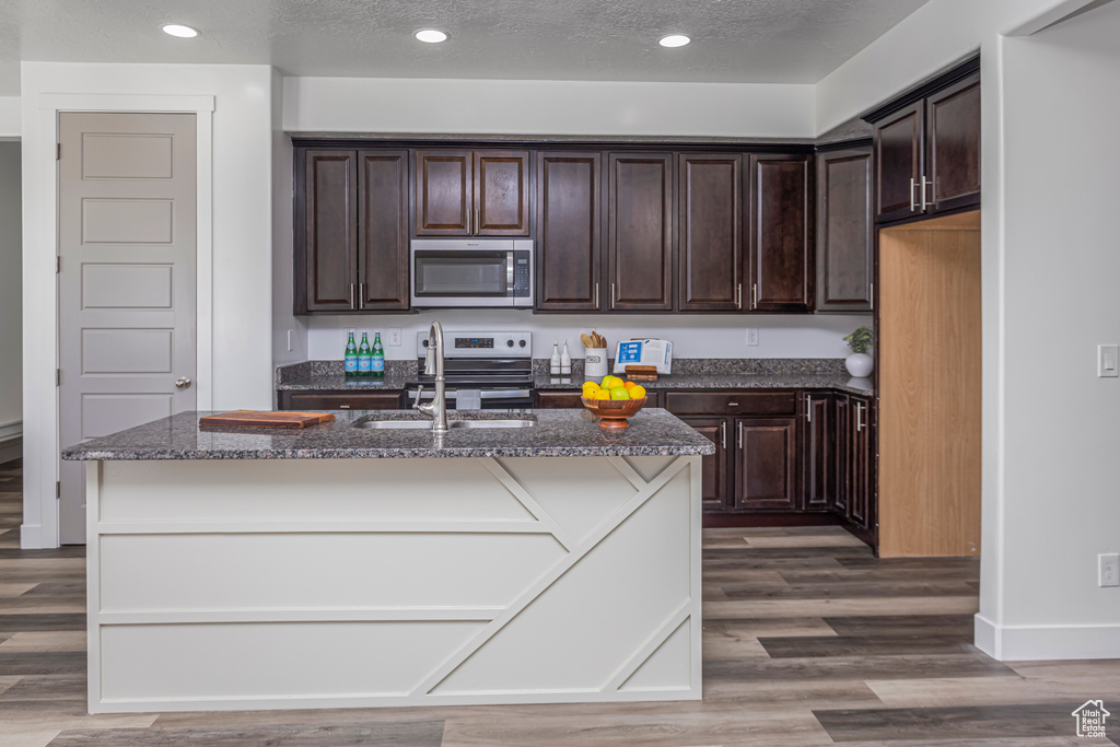 Kitchen with dark stone counters, a sink, appliances with stainless steel finishes, dark brown cabinets, and wood finished floors
