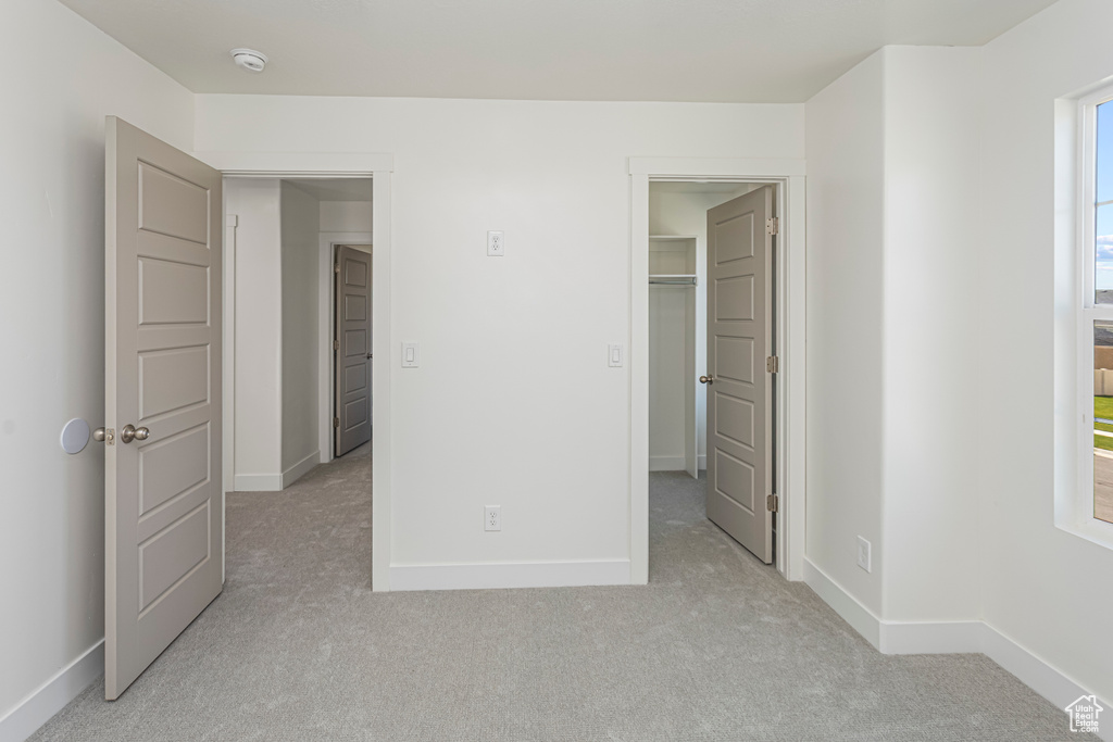 Unfurnished bedroom with baseboards, light carpet, and a spacious closet