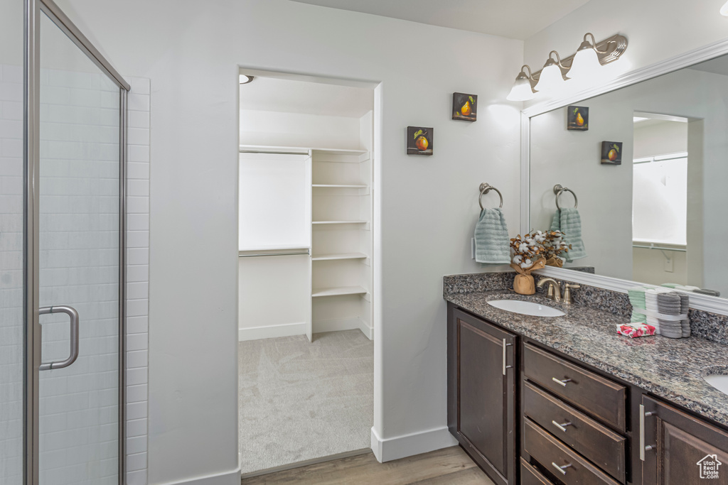 Full bathroom with wood finished floors, a shower stall, double vanity, a sink, and baseboards
