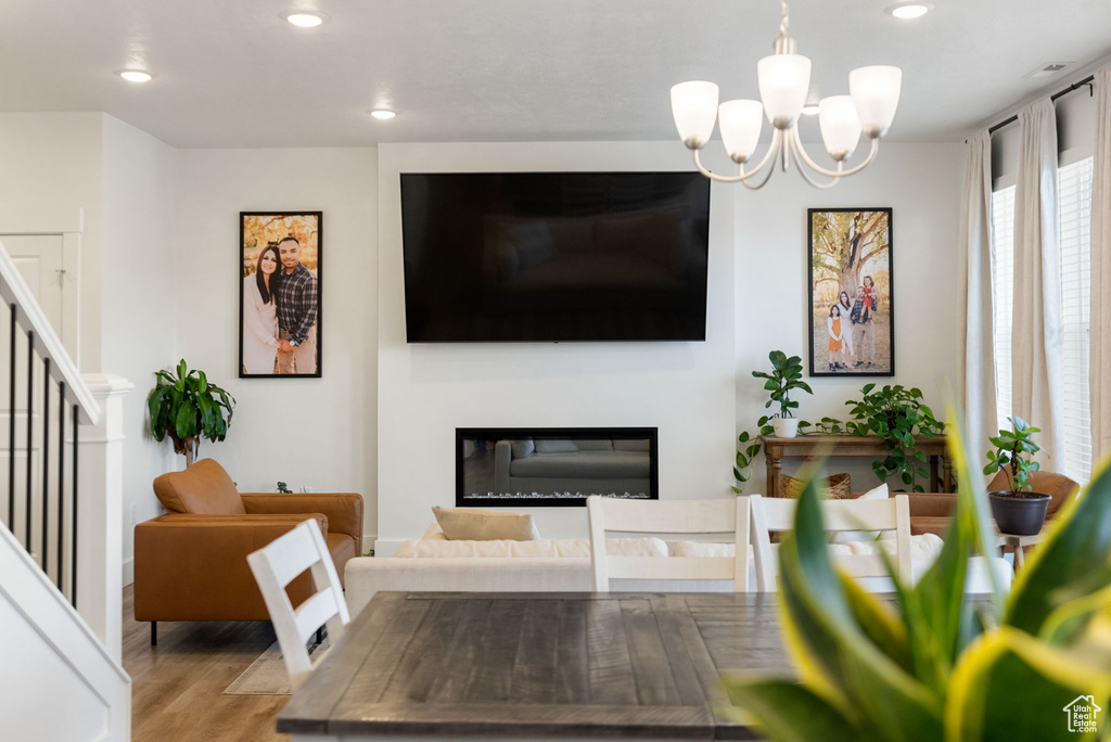 Living room with stairway, wood finished floors, a glass covered fireplace, an inviting chandelier, and recessed lighting