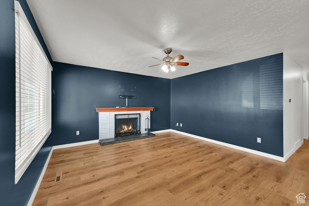 Unfurnished living room featuring a ceiling fan, baseboards, wood finished floors, and a fireplace