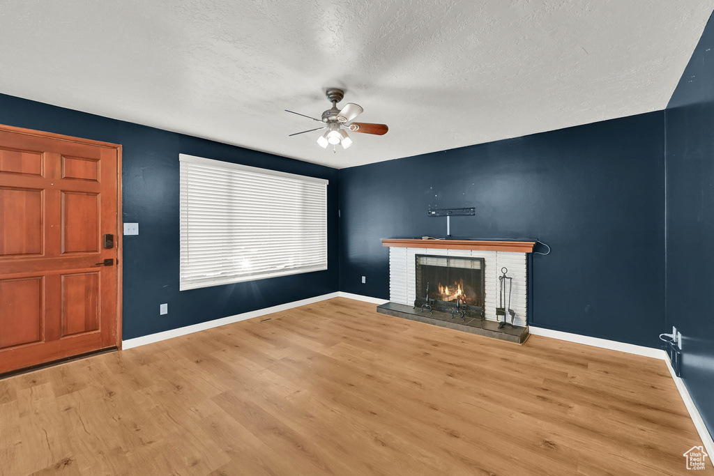 Unfurnished living room featuring a textured ceiling, a brick fireplace, ceiling fan, and wood finished floors
