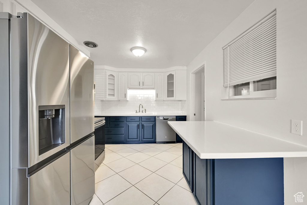 Kitchen featuring a sink, light countertops, blue cabinetry, stainless steel appliances, and glass insert cabinets
