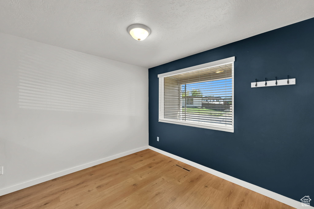 Spare room with visible vents, a textured ceiling, baseboards, and wood finished floors