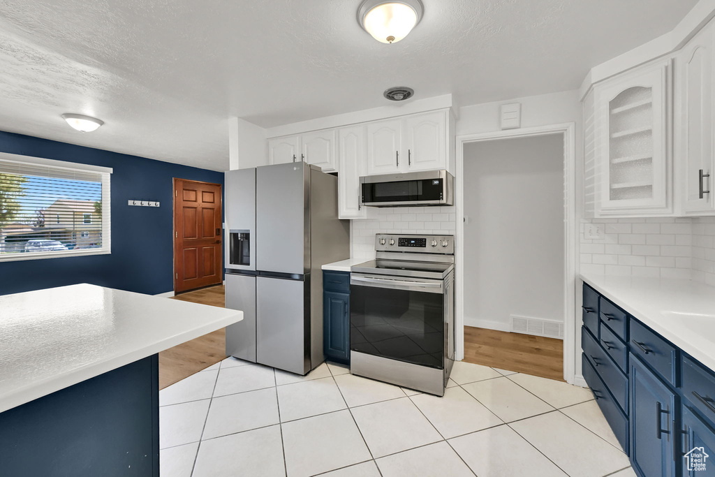 Kitchen featuring light countertops, white cabinets, tasteful backsplash, blue cabinets, and appliances with stainless steel finishes