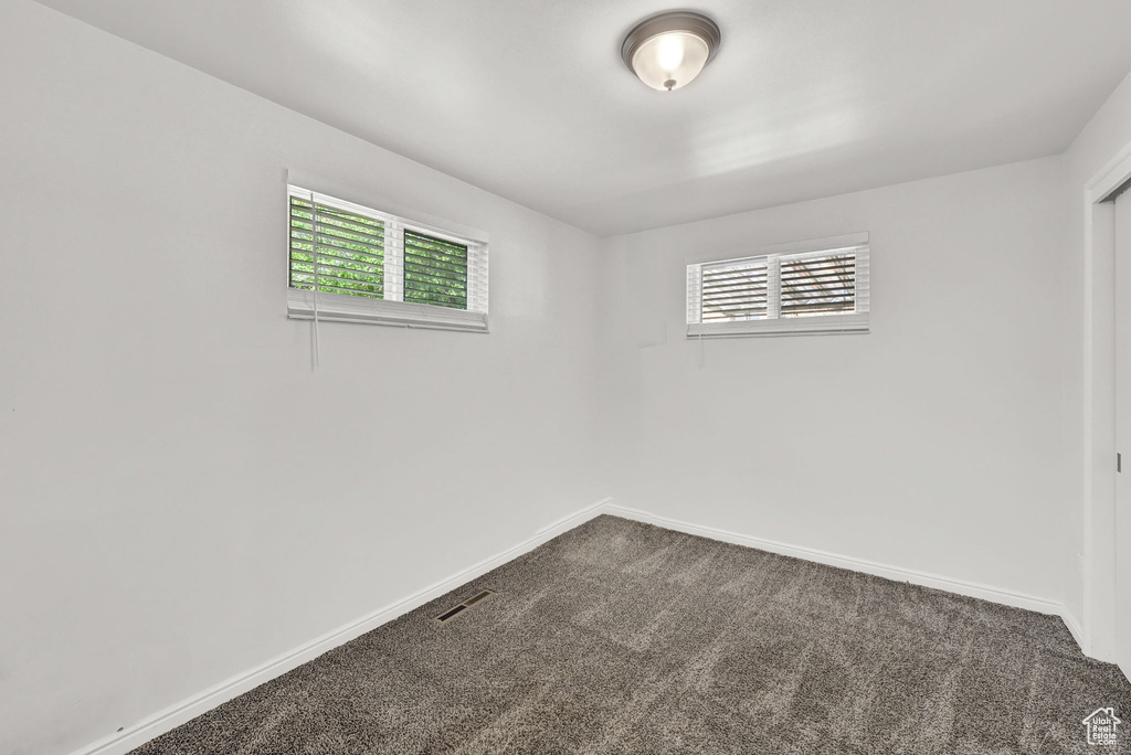 Empty room featuring plenty of natural light, baseboards, dark carpet, and visible vents