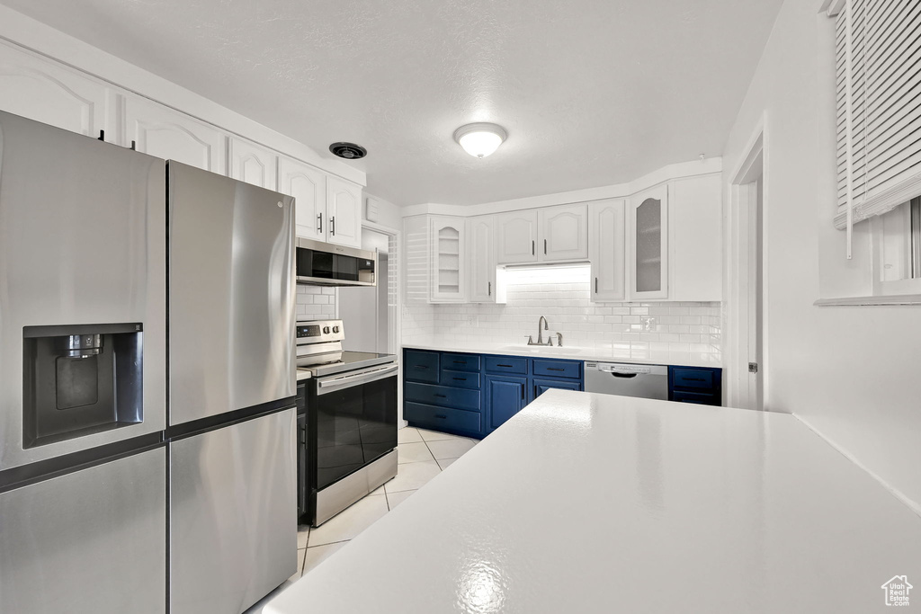 Kitchen with decorative backsplash, white cabinetry, blue cabinets, a sink, and stainless steel appliances