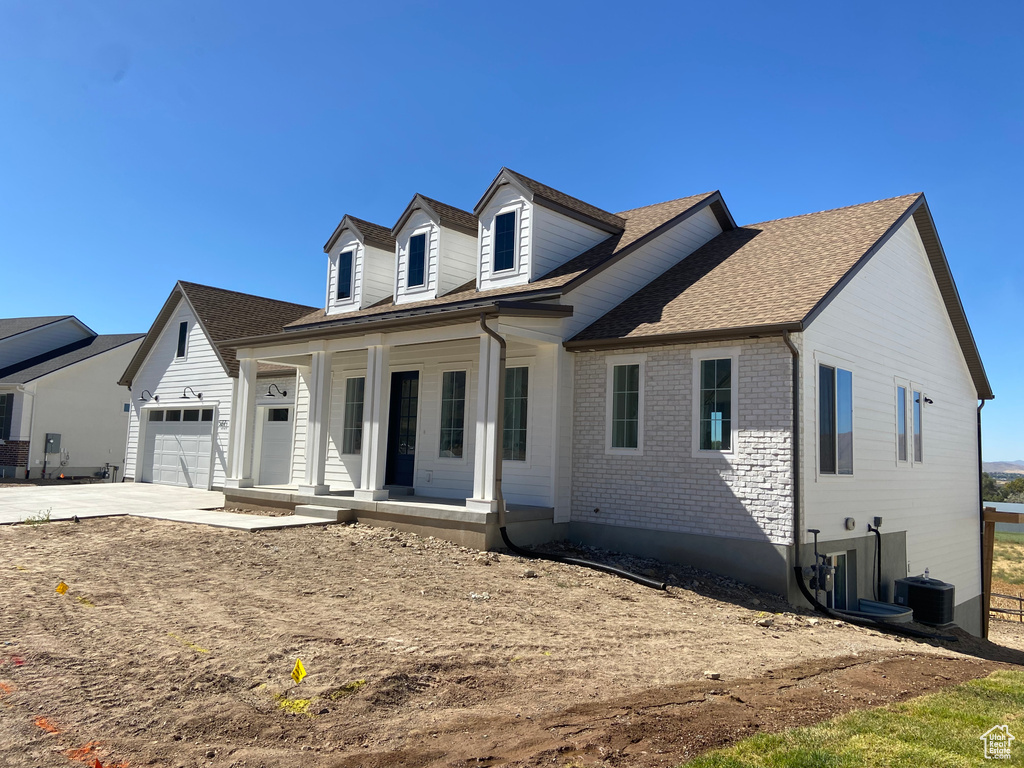 Cape cod home with central AC unit, concrete driveway, a shingled roof, a porch, and a garage