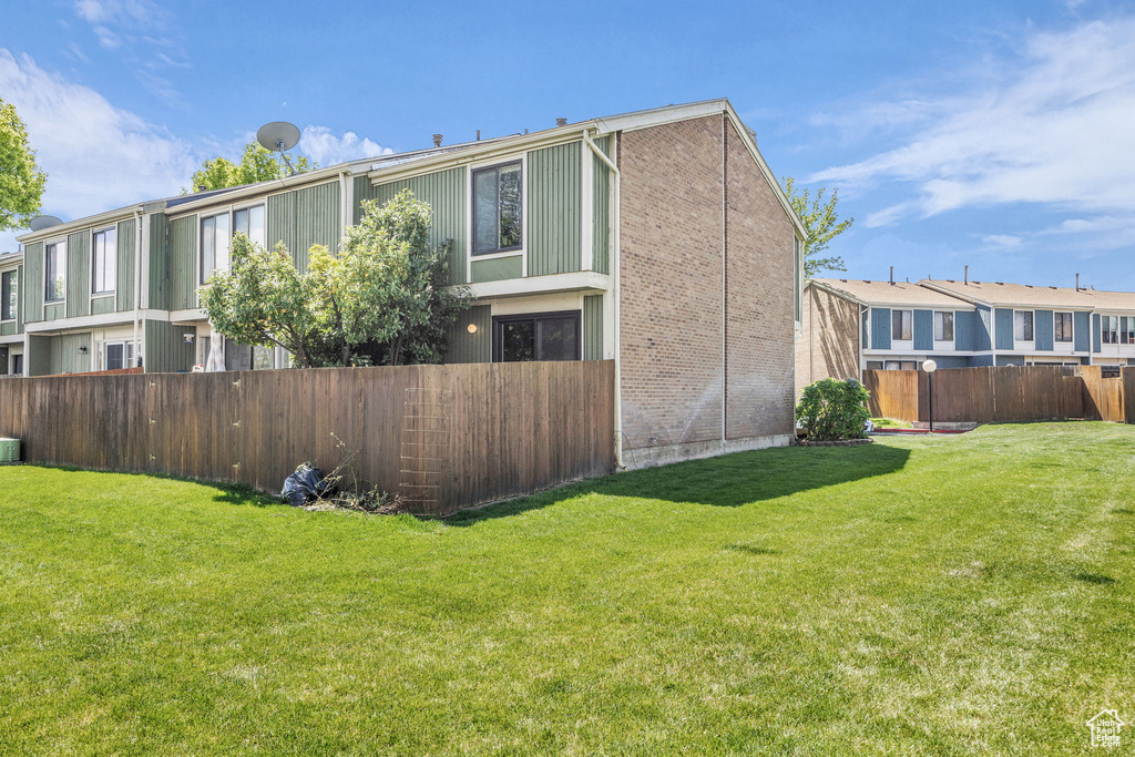 View of property exterior with brick siding, a fenced backyard, and a lawn