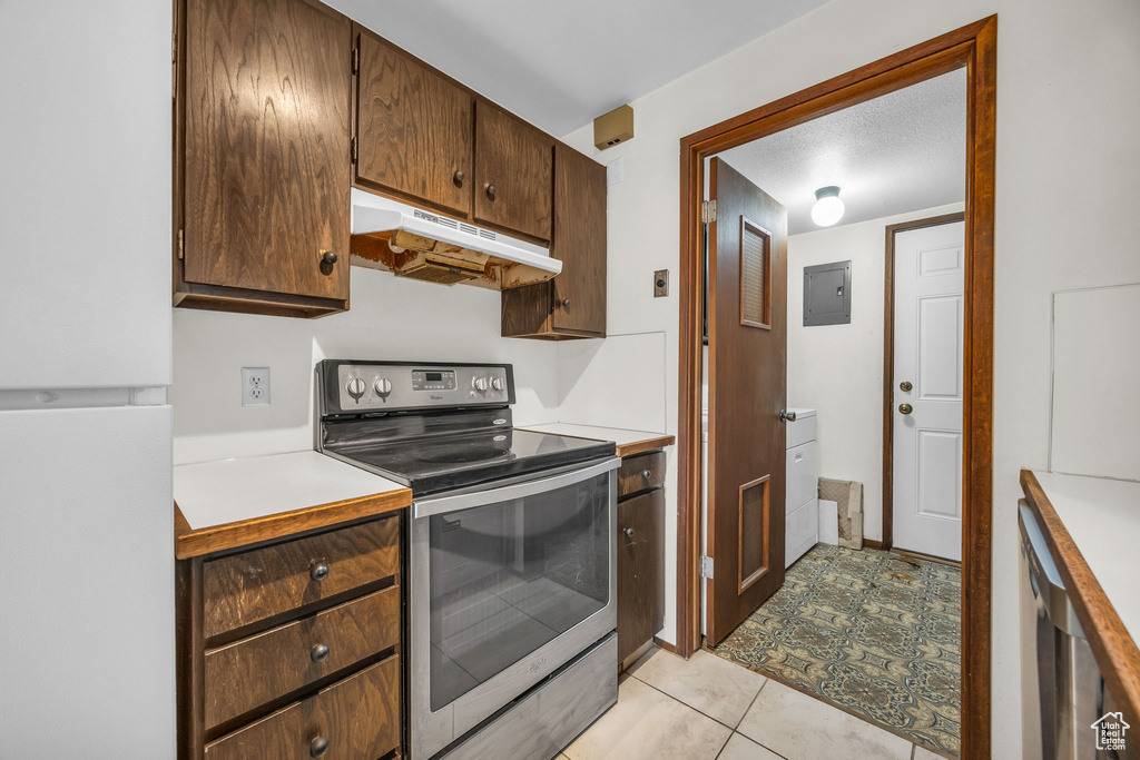 Kitchen featuring freestanding refrigerator, electric range, under cabinet range hood, light countertops, and electric panel