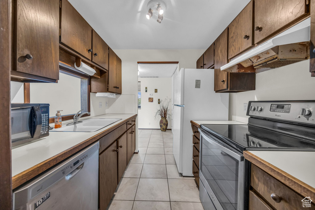 Kitchen with light countertops, a sink, stainless steel appliances, and under cabinet range hood