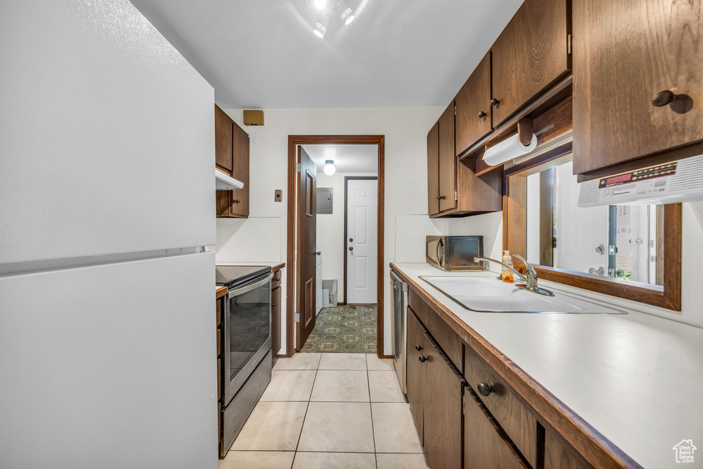 Kitchen featuring a sink, light countertops, freestanding refrigerator, under cabinet range hood, and electric range