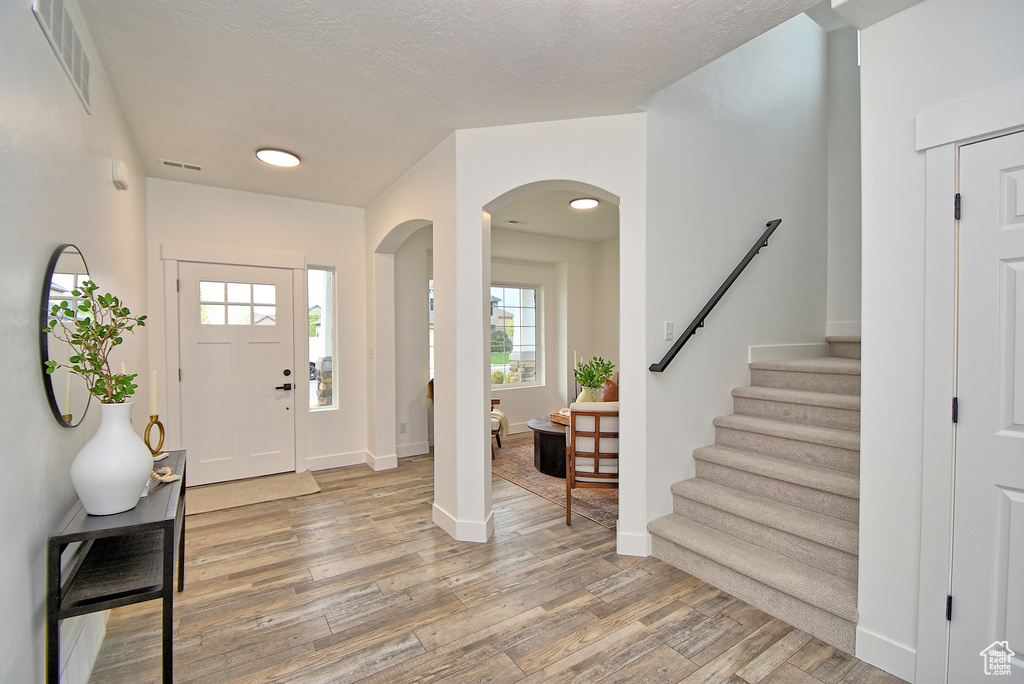 Foyer entrance featuring stairway, visible vents, baseboards, arched walkways, and light wood-type flooring