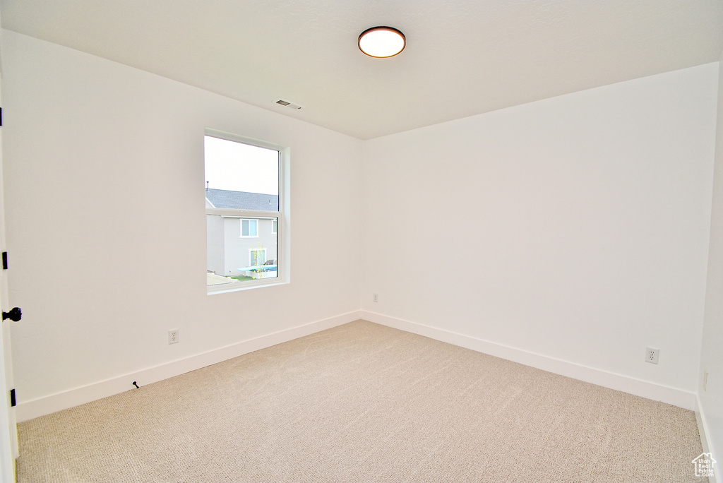 Empty room featuring baseboards, visible vents, and light colored carpet