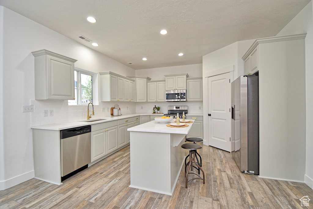 Kitchen with light wood-style flooring, stainless steel appliances, light countertops, a kitchen island, and a sink