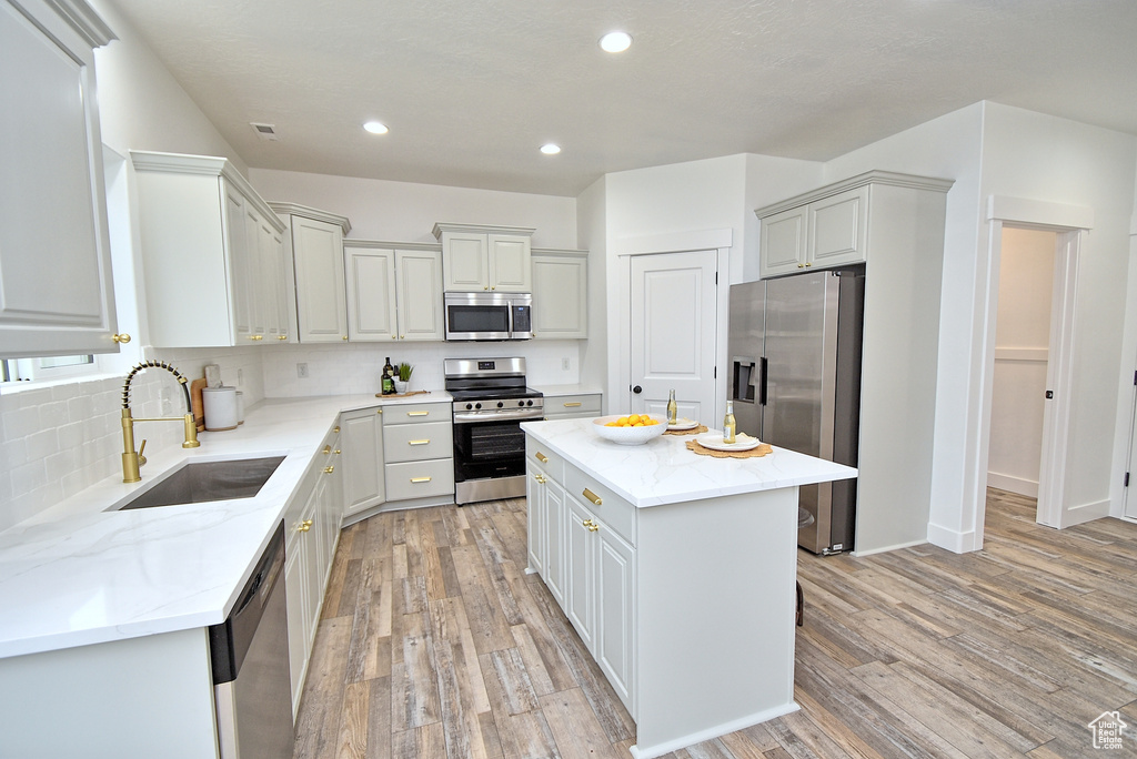 Kitchen featuring a sink, stainless steel appliances, tasteful backsplash, light stone counters, and a kitchen island