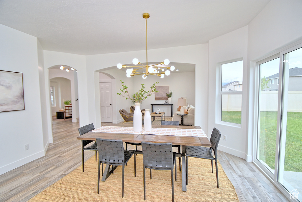 Dining room featuring baseboards, light wood-style flooring, arched walkways, and a notable chandelier