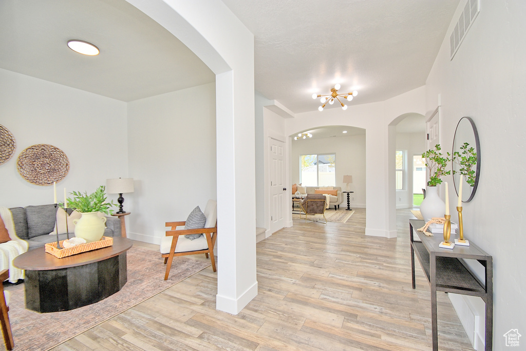 Foyer entrance with visible vents, light wood-style floors, baseboards, an inviting chandelier, and arched walkways