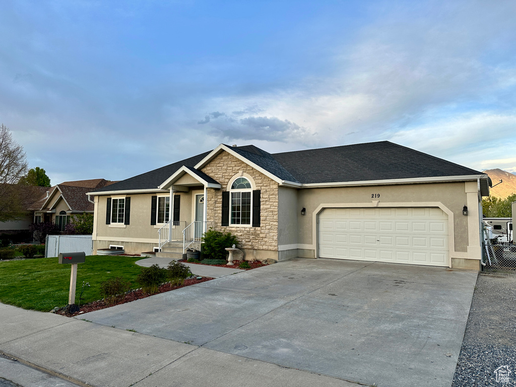 Ranch-style home featuring stucco siding, stone siding, a front lawn, concrete driveway, and an attached garage
