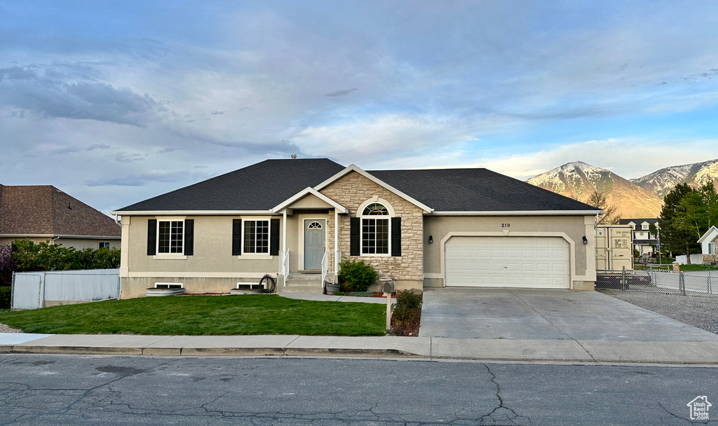 Ranch-style home with a front yard, a garage, a mountain view, stucco siding, and fence