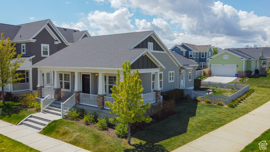 View of front facade with a residential view, covered porch, fence, board and batten siding, and a front yard