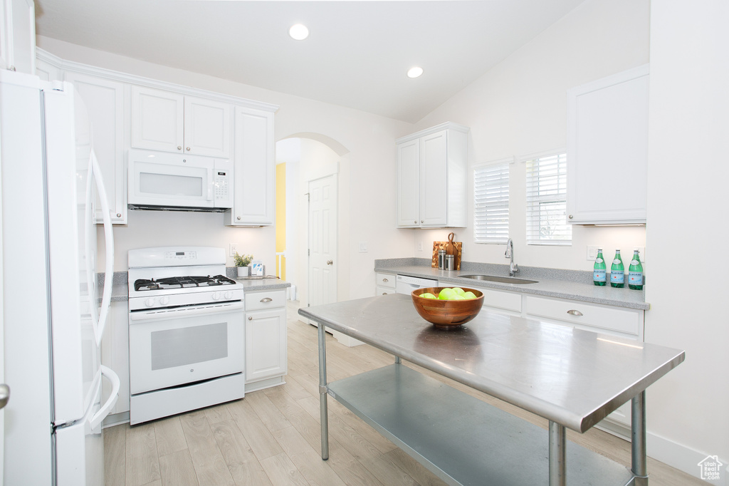 Kitchen with white cabinets, white appliances, a sink, and light wood-style floors
