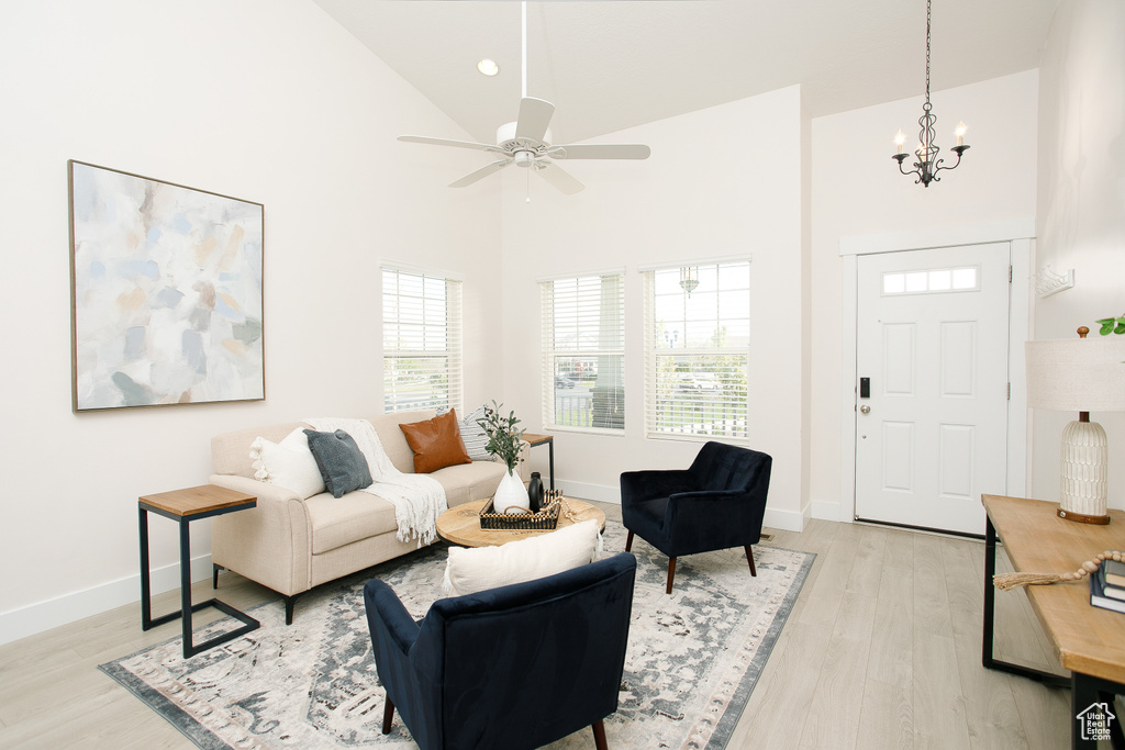 Living area featuring light wood finished floors, baseboards, recessed lighting, ceiling fan with notable chandelier, and high vaulted ceiling