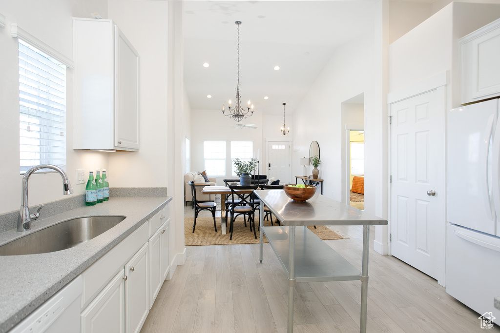 Kitchen with light wood-style floors, a notable chandelier, a sink, and white appliances
