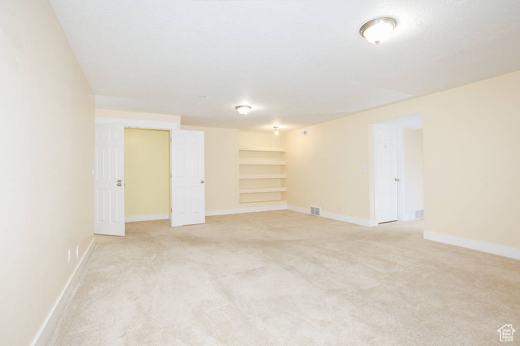 Basement featuring baseboards, built in shelves, and light colored carpet