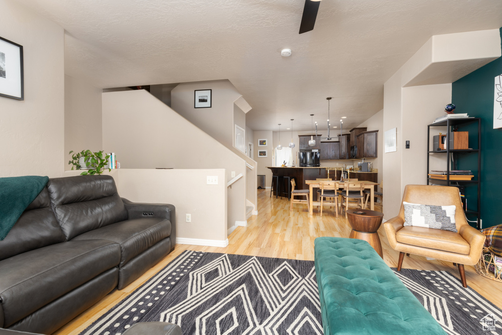 Living room featuring baseboards, a ceiling fan, light wood finished floors, and stairway