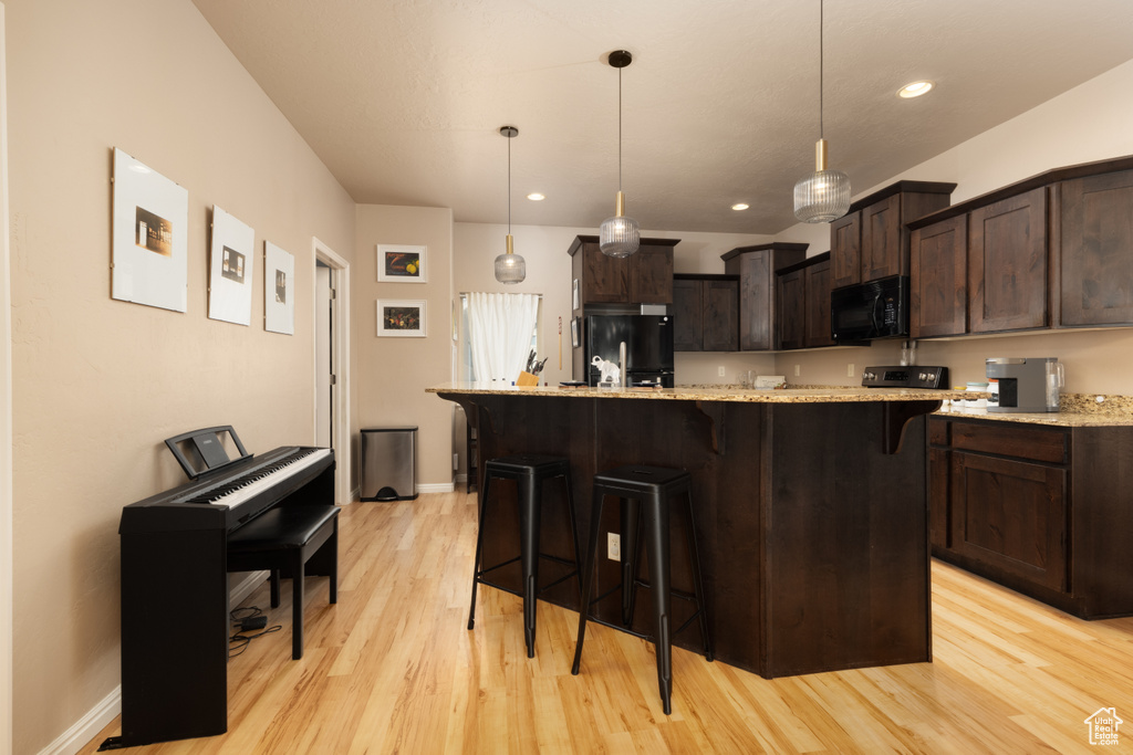 Kitchen with a breakfast bar area, dark brown cabinetry, light stone counters, black appliances, and light wood finished floors