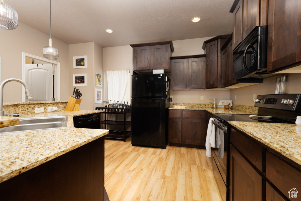 Kitchen featuring dark brown cabinetry, light wood-type flooring, a sink, black appliances, and decorative light fixtures