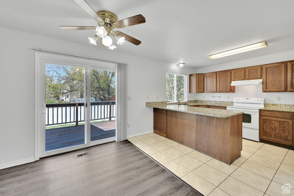 Kitchen featuring light stone countertops, a sink, under cabinet range hood, white electric range oven, and a peninsula