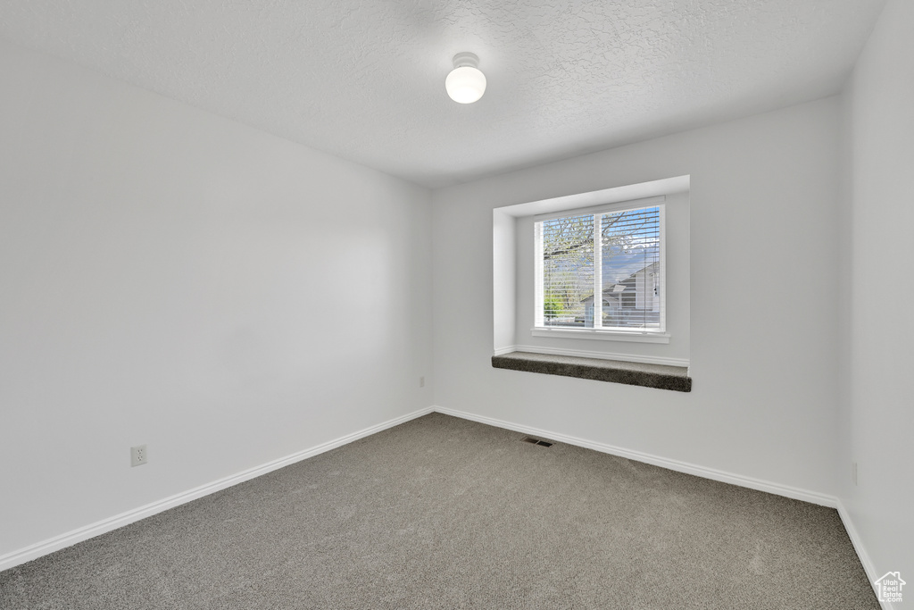 Carpeted empty room with a textured ceiling, visible vents, and baseboards