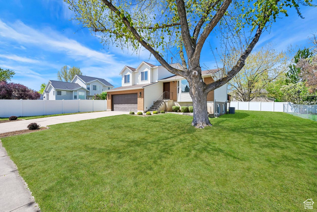 View of front facade with a front lawn, driveway, brick siding, an attached garage, and fence