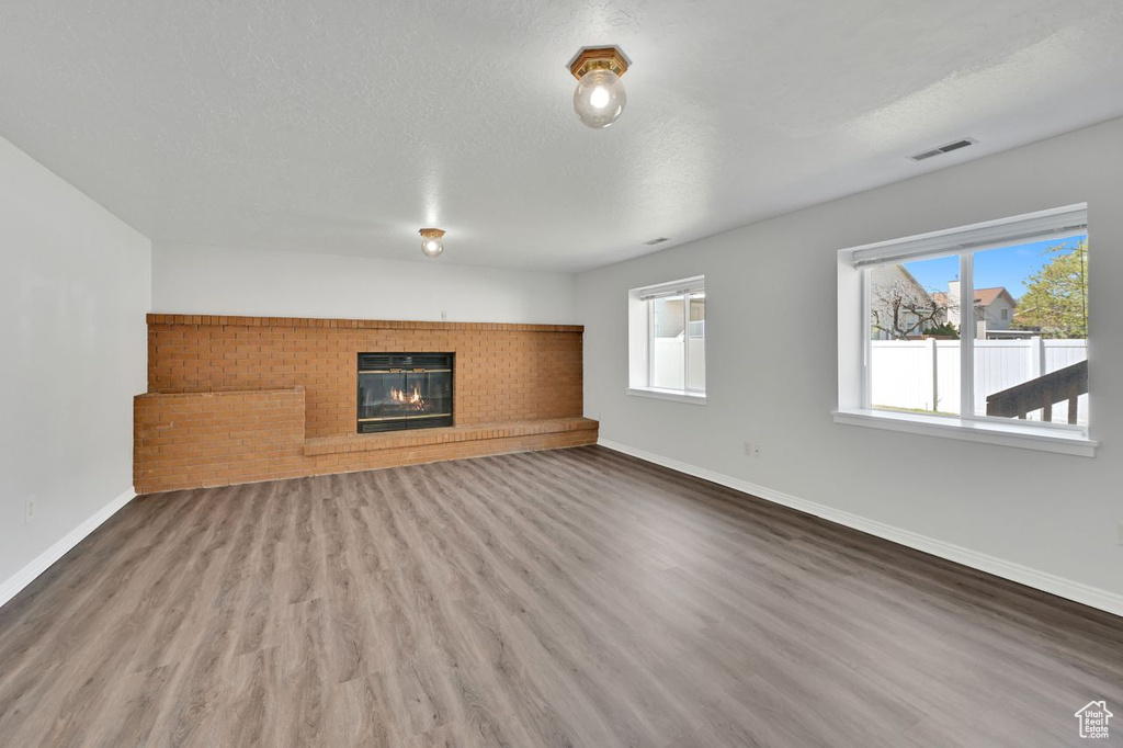 Unfurnished living room featuring a glass covered fireplace, visible vents, wood finished floors, and baseboards