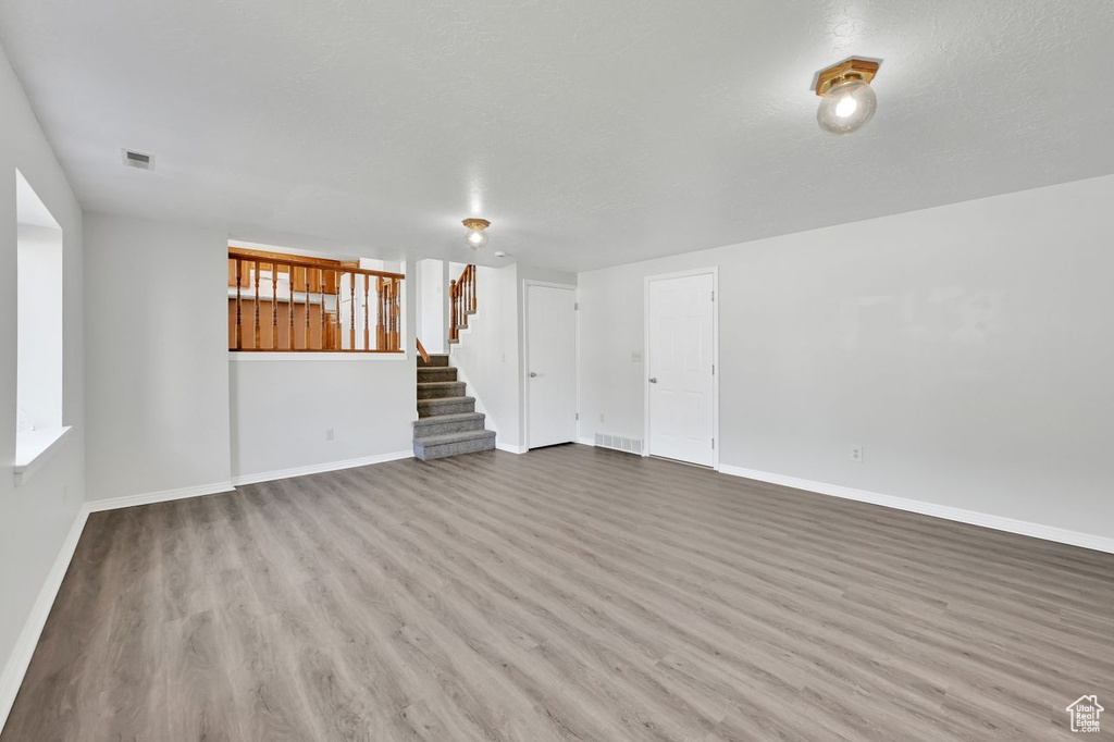 Unfurnished living room with visible vents, stairway, wood finished floors, and baseboards