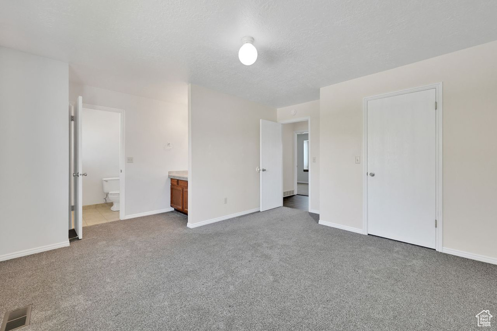 Unfurnished bedroom with ensuite bath, carpet floors, baseboards, visible vents, and a textured ceiling