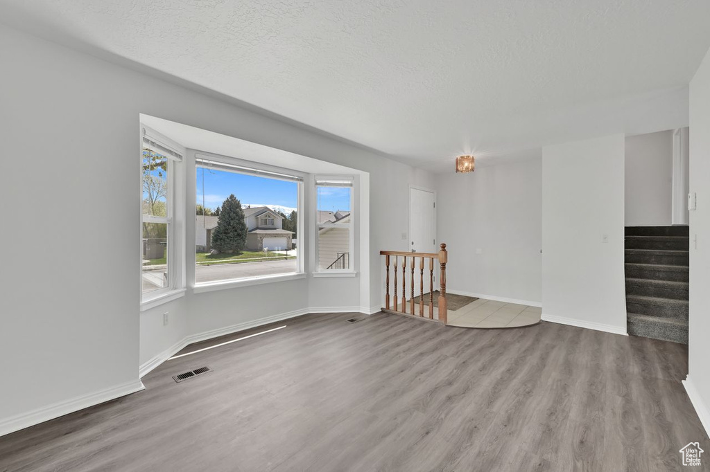 Unfurnished living room featuring wood finished floors, stairs, baseboards, visible vents, and a textured ceiling