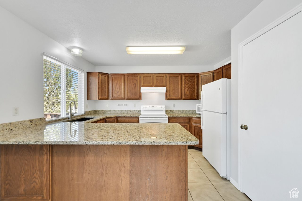 Kitchen with a sink, under cabinet range hood, stove, a peninsula, and freestanding refrigerator
