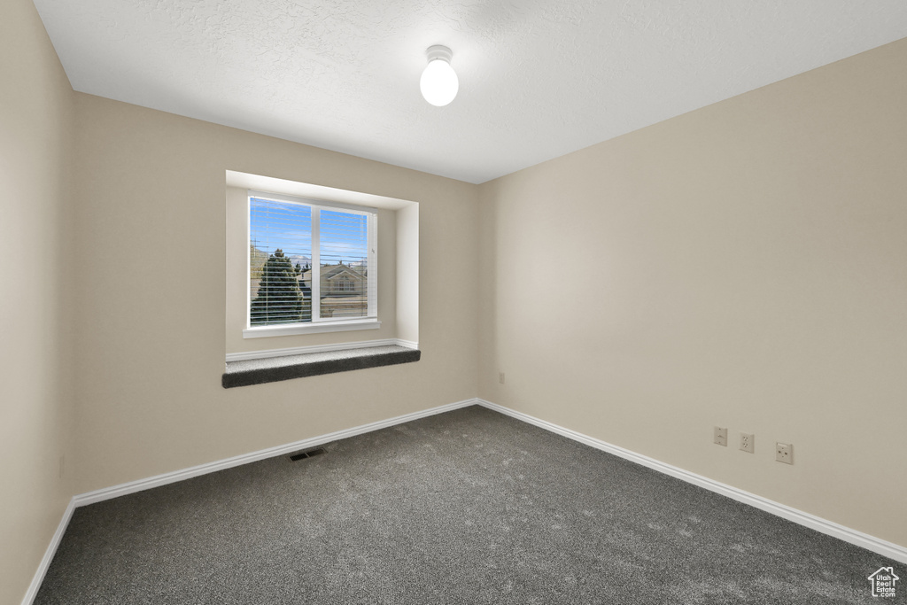 Unfurnished room featuring dark carpet, visible vents, and baseboards