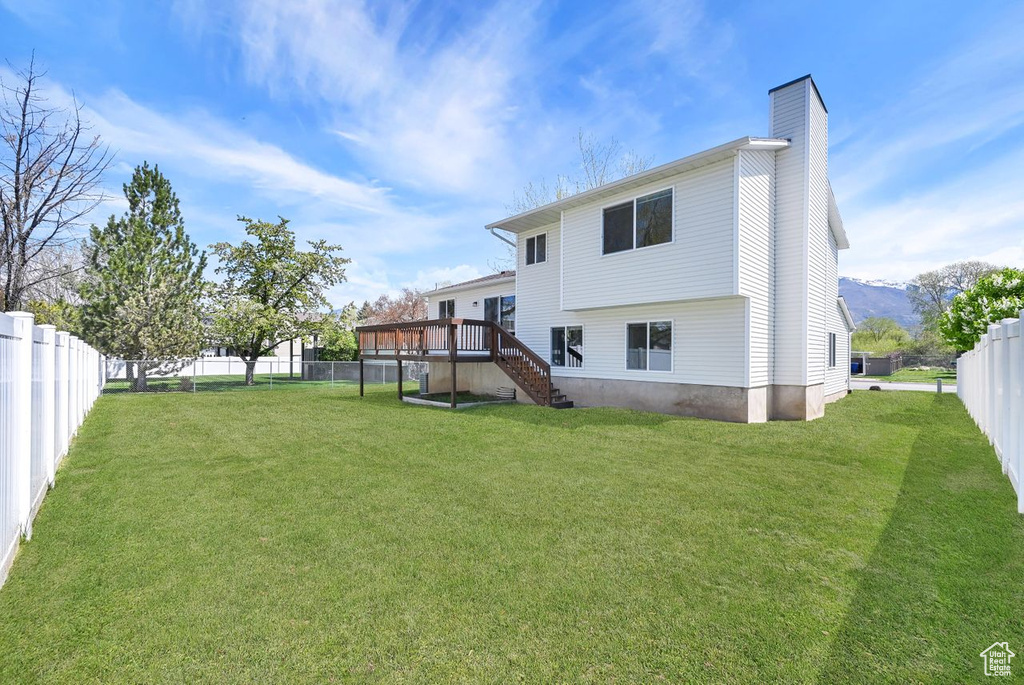 Back of property with a chimney, a deck, a lawn, stairway, and a fenced backyard