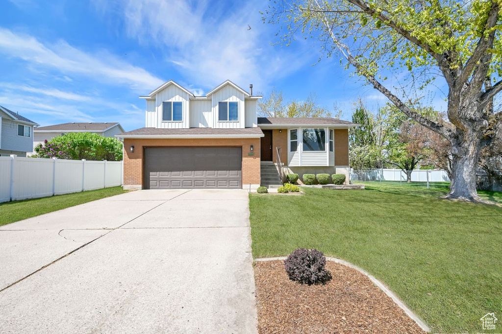 Split level home with fence, concrete driveway, and brick siding