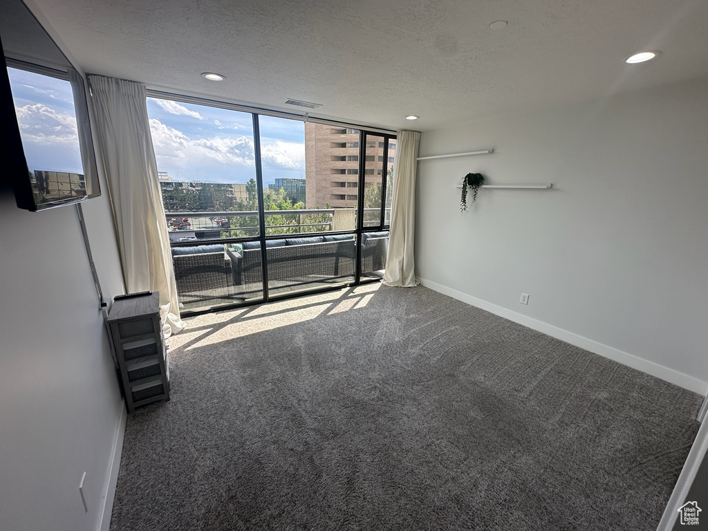 Carpeted empty room featuring visible vents, a wall of windows, baseboards, and a textured ceiling