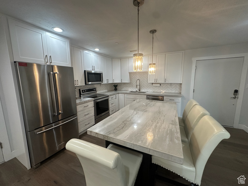Kitchen with stainless steel appliances, a sink, white cabinetry, decorative backsplash, and dark wood-type flooring
