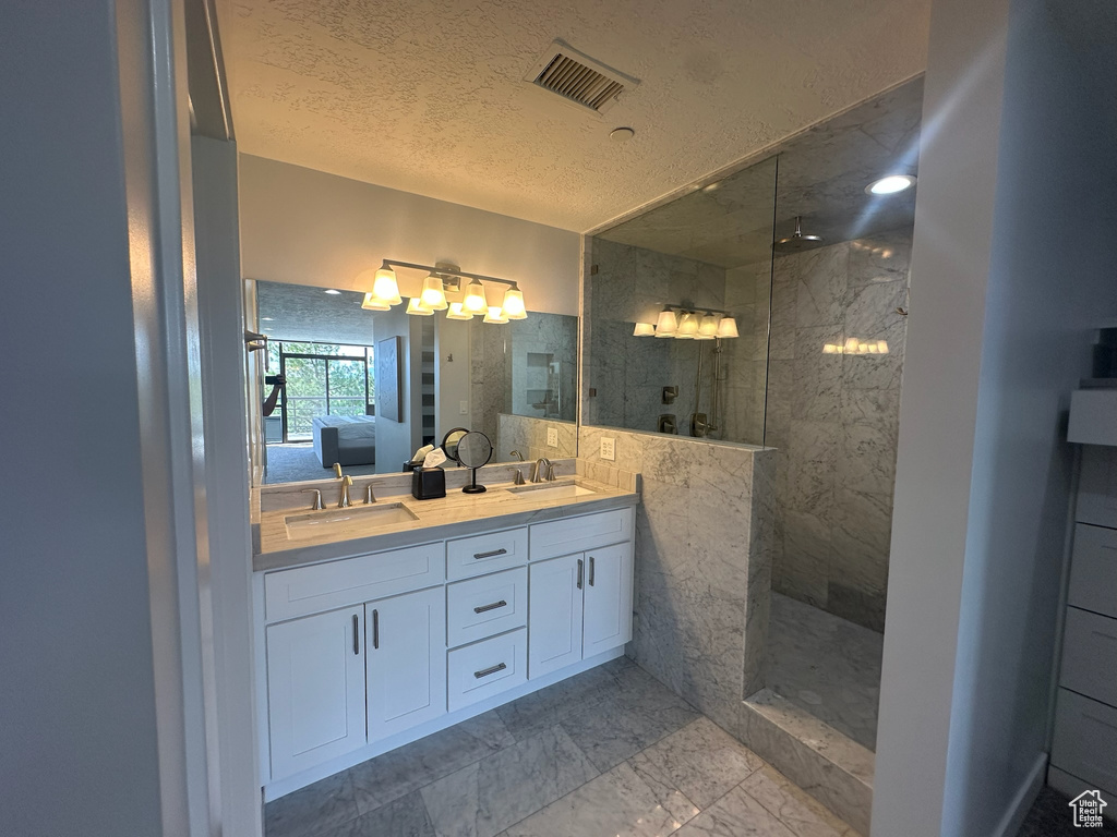 Full bathroom featuring a marble finish shower, a sink, visible vents, and double vanity