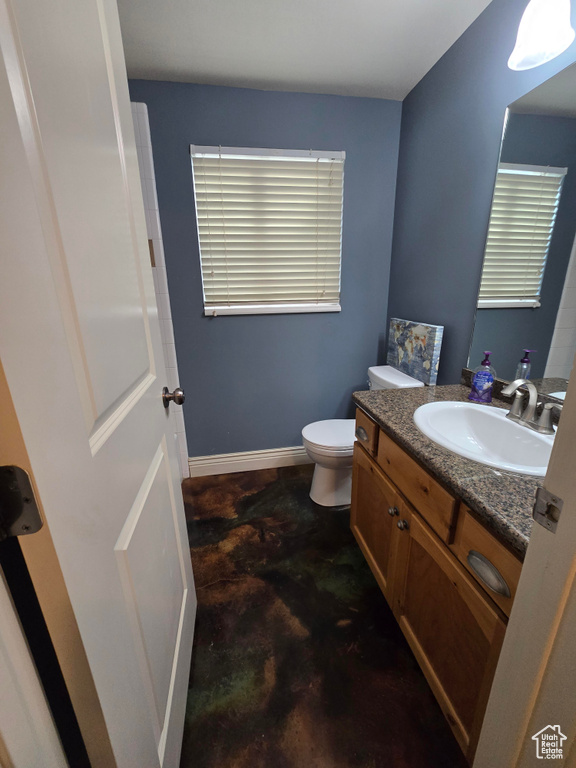 Half bath with toilet, vanity, concrete flooring, and baseboards