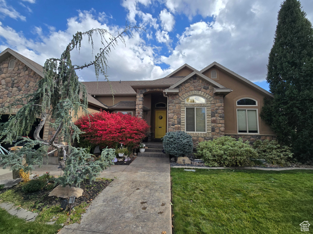 Ranch-style home featuring a front lawn, stone siding, and a shingled roof