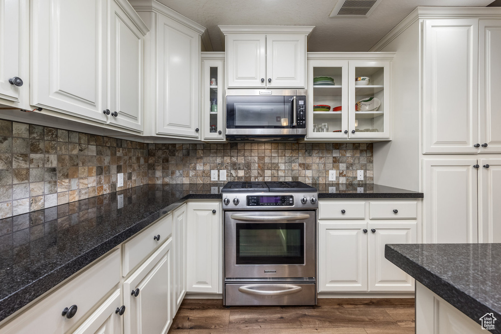 Kitchen featuring stainless steel appliances, white cabinetry, glass insert cabinets, and backsplash